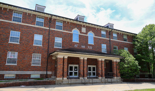 Exterior view of Bradley Hall, a multi-story brick residence hall with a central entrance, large windows, and a landscaped courtyard.
