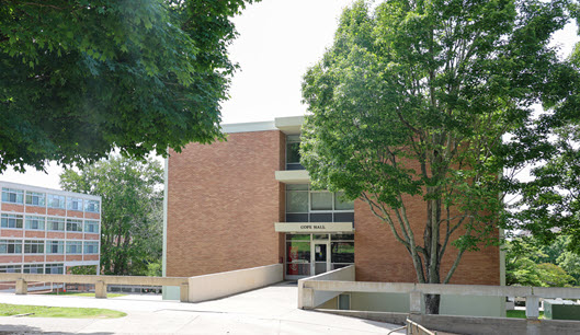 Exterior view of Cope Hall, a multi-story brick residence hall with a central entrance, large windows, and a landscaped courtyard.