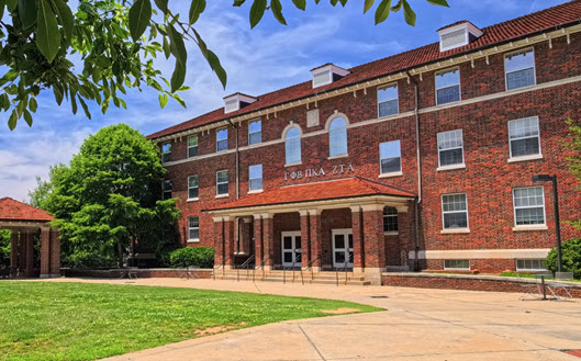 Exterior view of Wannamaker Hall, a multi-story brick residence hall with a central entrance, large windows, and a landscaped courtyard.