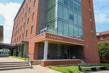 Exterior view of Cribb Hall, a multi-story brick residence hall with a central entrance, large windows, and a landscaped courtyard.