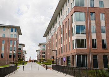 Exterior view of Douthit Hills D, a multi-story brick residence hall with a central entrance, large windows, and a landscaped courtyard.