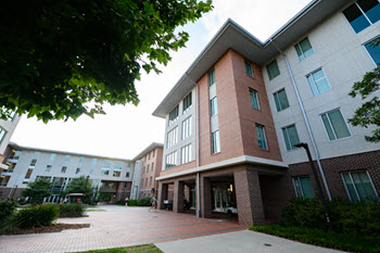 Exterior view of Douthit Hills F, a multi-story brick residence hall with a central entrance, large windows, and a landscaped courtyard.