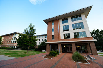 Exterior view of Douthit Hills G, a multi-story brick residence hall with a central entrance, large windows, and a landscaped courtyard.