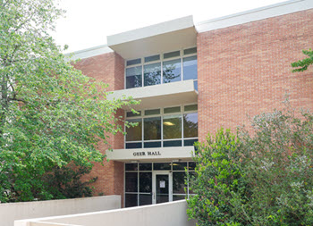Exterior view of Geer Hall, a multi-story brick residence hall with a central entrance, large windows, and a landscaped courtyard.