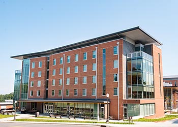 Exterior view of Gressette Hall, a multi-story brick residence hall with a central entrance, large windows, and a landscaped courtyard.