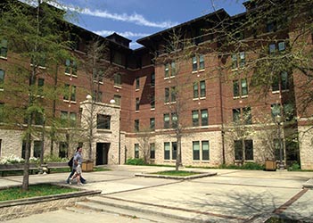 Exterior view of Holmes Hall, a multi-story brick residence hall with a central entrance, large windows, and a landscaped courtyard.