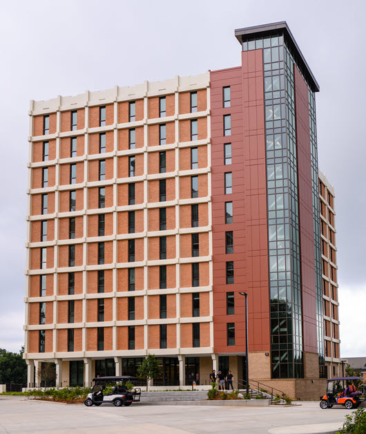 Exterior view of Lever Hall, a multi-story brick residence hall with a central entrance, large windows, and a landscaped courtyard.