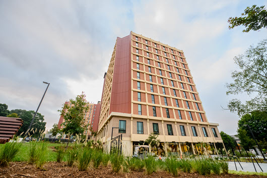 Exterior view of Manning Hall, a multi-story brick residence hall with a central entrance, large windows, and a landscaped courtyard.