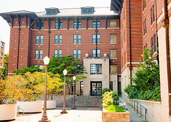 Exterior view of McCabe Hall, a multi-story brick residence hall with a central entrance, large windows, and a landscaped courtyard.