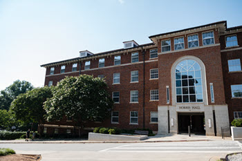 Exterior view of Norris Hall, a multi-story brick residence hall with a central entrance, large windows, and a landscaped courtyard.
