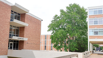 Exterior view of Sanders Hall, a multi-story brick residence hall with a central entrance, large windows, and a landscaped courtyard.