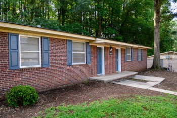 Exterior view of Thornhill Village, a single-story residential building with multiple entry doors, shutters, and a shaded lawn with trees.