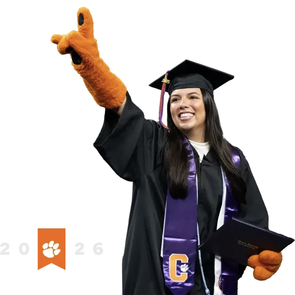 student in regalia and tiger gloves holds up her index finger as she smiles. The year 2026 is displayed along with an orange ribbon with the Clemson tiger paw logo.