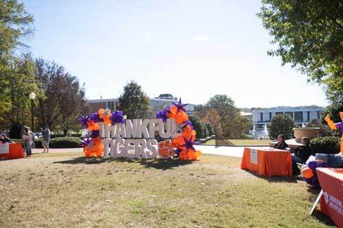 A large white sign that says 'Thankful Tigers' with orange and purple balloons on each side.