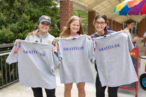 Three students posing together while holding up gray Clemson 'Gratitude' shirts.